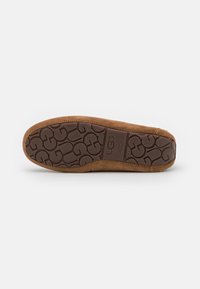Bruine suède schapenleren schoen met een gestructureerde rubberen zool, voorzien van een kenmerkend looppatroon en UGG-branding die op de zijkant is geperst.