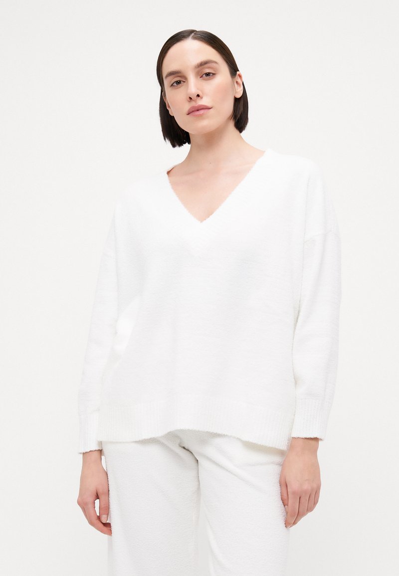White oversized sweater with a V-neckline, ribbed cuffs, and hem. Soft, textured fabric with a relaxed fit. Paired with matching white pants.