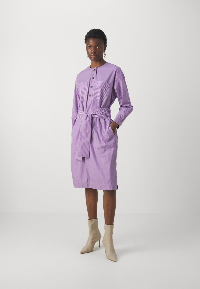 Purple striped shirt dress with long sleeves, button front, chest pockets, and a tied waist. Worn with beige ankle boots.