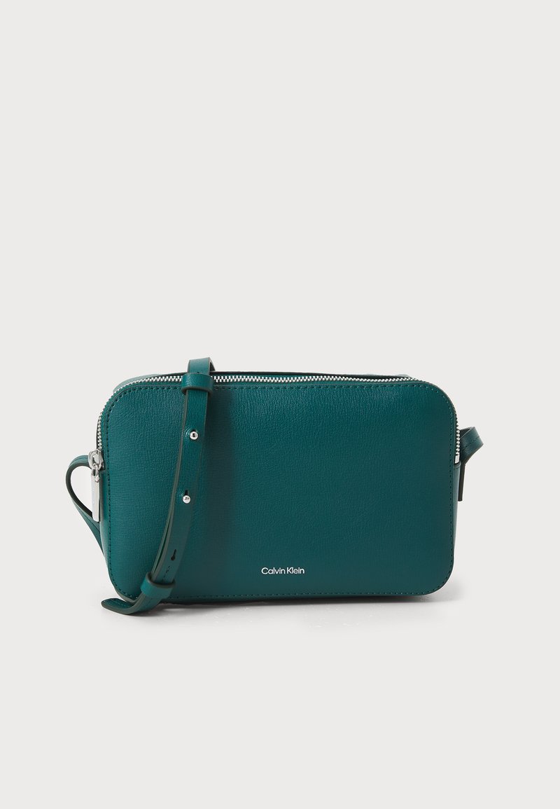 Turkusowa skórzana prostokątna torebka na ramię z zamknięciem na zamek błyskawiczny, regulowanym paskiem oraz wytłoczonym logo marki z przodu. Gładka faktura.