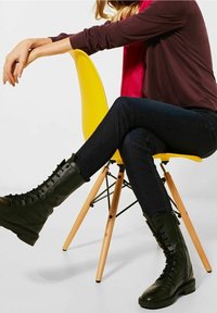 Czarne, do kolan sięgające buty wojskowe z teksturowanej skóry, z wiązaniem na przodzie i solidną podeszwą, zestawione z ciemnoniebieskimi jeansami i burgundową bluzką.