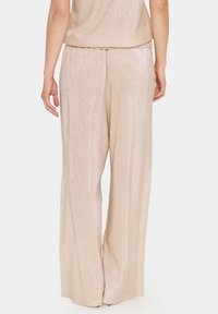 Wide-leg pants in a shimmery beige fabric, featuring a ribbed texture and elastic waist. The back shows a clean finish with minimal detailing.