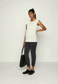 Top branco de manga curta com detalhes em ruffles, combinado com calças azul-marinho com bolinhas. Modelo segurando uma bolsa preta e usando sapatos pretos tipo slip-on.