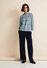 Ljusblå rutig topp med lång ärm, rund halsringning och avslappnad passform, kombinerad med marinblå vida byxor och svarta loafers.