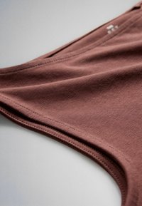 Gros plan d'un vêtement marron sans manches avec des coutures apparentes et un tissu en coton doux sur une surface claire.