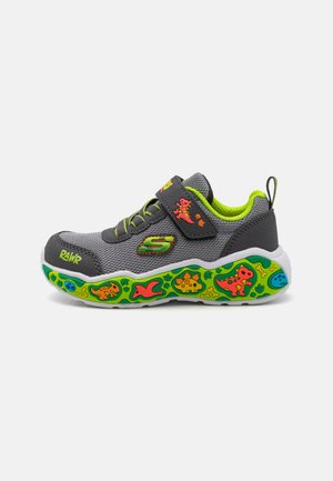 Zapatilla deportiva gris con una correa de Velcro, acentos verdes y una suela texturizada que presenta patrones coloridos de dinosaurios y animales.