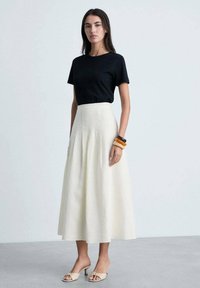 Tricou negru asortat cu o fustă cremoasă, cu talie înaltă, până la genunchi. Outfitul are un material fin și un design minimalistic. Accentuat cu brățări.