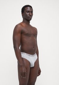 Boxeri gri din bumbac cu logo-ul Fila pe talie, având o croială confortabilă și un design simplu. Modelul stă în profil pe un fundal simplu.