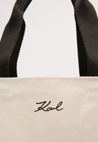 Torba tote z płótna w naturalnym kolorze z czarnymi materiałowymi uchwytami i haftowanym logo "Karl" w kursywie z przodu.