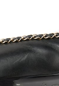 Gros plan d’un sac à main en cuir noir avec un détail de chaîne dorée et noire le long du bord supérieur.