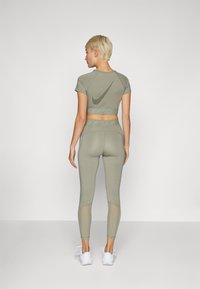 Oliven grønn Nike sport crop topp med korte ermer og mesh-detaljer, parret med matchende høytalede leggings med teksturerte paneler.