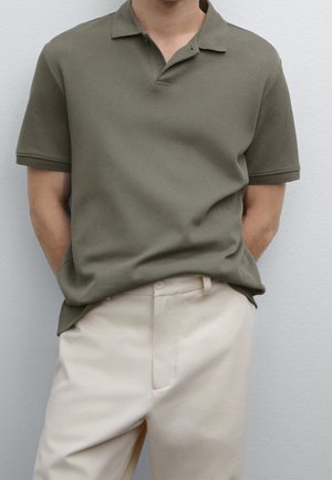 Olivgrünes Poloshirt aus strukturiertem Stoff, mit kurzen Ärmeln und einer dreiknöpfigen Blende, kombiniert mit hellbeigen Hosen.