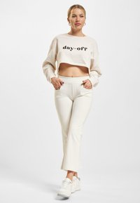 Kuttet beige hettegenser med "day-off" tekst, kombinert med tettsittende hvite bukser. Modellen har på seg hvite sneakers, og viser en avslappet antrekk.