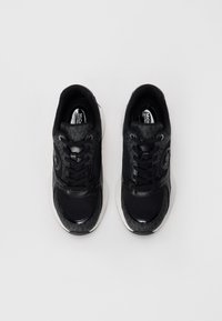 Black sneakers with a combination of glossy and textured materials, featuring a white midsole and black laces, designed with a round toe.
