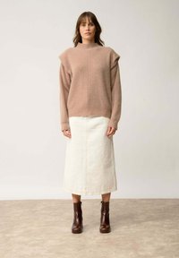 Lichtroze gebreide trui met hoge hals, ontspannen mouwen; gecombineerd met een crèmekleurige denimrok en bruine enkellaarsjes. Textuurdetails zichtbaar.