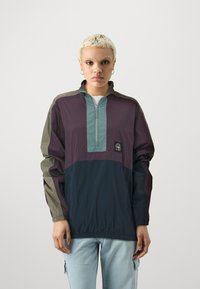 Pullover jacket featuring a quarter-zip front, color-blocked design in dark purple, green, and navy, with elastic cuffs and minor logo detail.