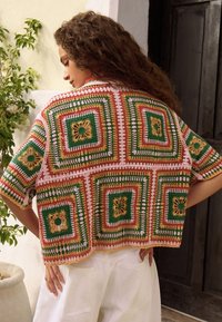 Top de crochet con patrones cuadrados multicolores en verde, naranja y rosa, con motivos florales, mangas cortas y un ajuste holgado.