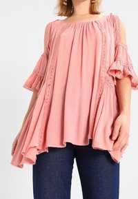 Růžová blůza s odhalenými rameny, volánkovými rukávy, krajkovými detaily a volným střihem. Nosit s modrými džínami. Měkká, lehká tkanina.