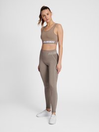 Top sportivo marrone a coste e leggings abbinati, con logo del marchio e linee di accento bianche, abbinati a sneakers bianche.