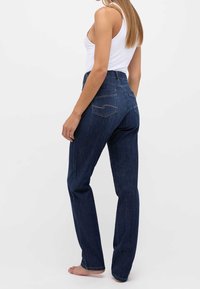 Jeans de tiro alto en azul oscuro con corte recto, que cuentan con bolsillos traseros con detalles de costura curvada. Textura de denim suave.