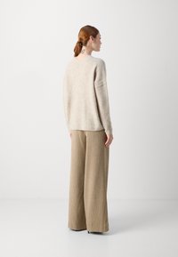 Beige knitted sweater with a relaxed fit, paired with wide-legged, ribbed, brown pants featuring vertical stripes.