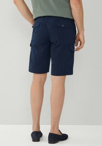 Pantaloni cargo blu navy realizzati in tessuto leggero, dotati di due tasche posteriori e tasche laterali. Indossati con calzature scure.