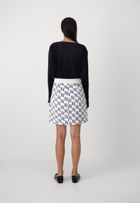 Czarna plisowana bluzka z długim rękawem połączona z białą spódnicą z czarnym geometrycznym wzorem. Dopasowany krój, do kolan, z czarnymi butami.