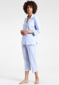 Vaaleansininen ja valkoinen raidallinen pyjamapukusetti, johon kuuluu nappilukollinen paita, jossa on tasku, ja croppatut housut, valmistettu pehmeästä kankaasta.