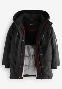 Veste noire imperméable avec capuche, accents rouges, plusieurs poches zippées et doublure matelassée à motif écossais.
