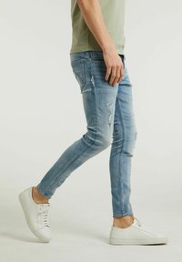 Ljust blå skinny jeans med slitna detaljer, visade tillsammans med en åtsittande ljusgrön t-shirt och vita sneakers, med en slät textur.