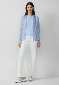 Lichtblauwe katoenen t-shirt, gelaagd onder een gestreepte blauwe en witte overhemd, gecombineerd met witte wijde broek en grijze sneakers.