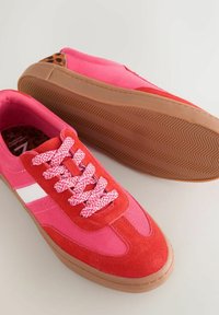 Sneakers i rød og lyserød ruskind, med hvide striber, lyserøde snørebånd og en gummisål med fiskebensmønster samt leopardprint indvendigt.