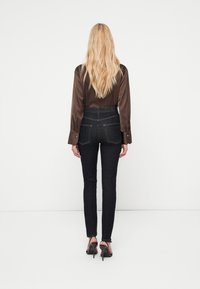 Blusa de satén marrón de manga larga combinada con jeans pitillo azul oscuro de tiro alto, con bolsillos traseros y un ajuste ceñido, complementada por zapatos de tacón alto.