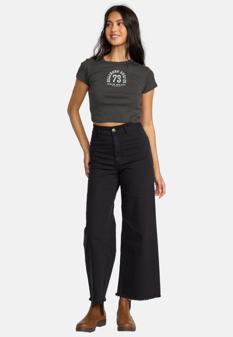 Gray cropped t-shirt with white graphic, paired with high-waisted black wide-leg jeans and brown ankle boots. Clean, modern styling.
