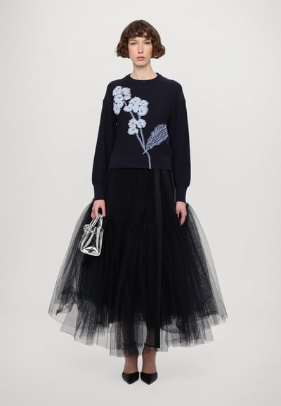 Navy knitted sweater with light blue floral embroidery paired with a voluminous black tulle skirt and a metallic handbag.
