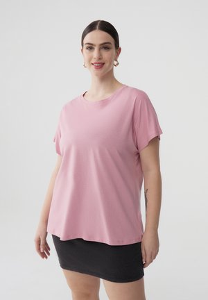 T-shirt rosa dalla vestibilità ampia, realizzato in un tessuto morbido, con scollatura rotonda e maniche corte. Indossato con una mini-gonna nera a costine.