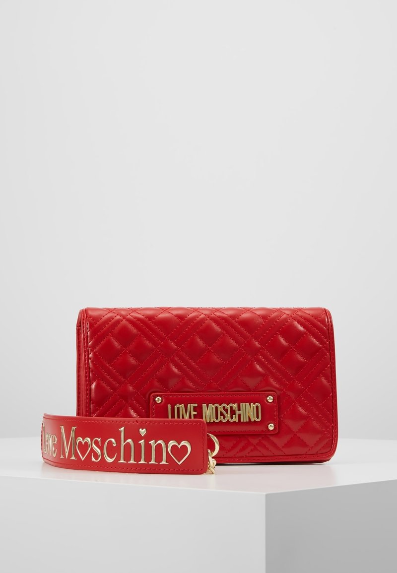 Sac à main matelassé rouge avec plaque dorée « LOVE MOSCHINO » et bandoulière détachable assortie avec texte doré embossé et décorations en forme de cœur.