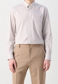 Vaaleanbeige pitkähihainen nappikauluspaita, jossa on pystysuorat valkoiset raidat, rinnassa tasku ja kalvosinyksityiskohdat. Yhdistetty beigenvärisiin housuihin.