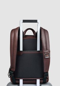 Mochila de cuero marrón con paneles texturizados negros, correas ajustables, asa superior y un detalle de metal con iniciales.