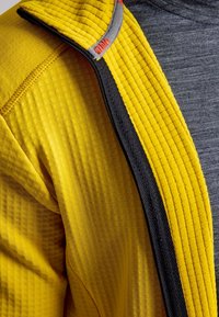 Yellow textured jacket with black zipper and inner gray fabric worn over a gray shirt.