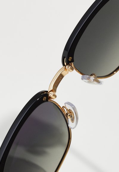 Black framed sunglasses with dark lenses, gold metal accents, and clear nose pads. Features a hinge connecting the two frames.