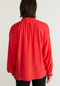 Röd långärmad blus med skräddarsydd hals och volangärmar. Mjukt tyg och lös passform. Har en nyckelhålsdetalj på baksidan.