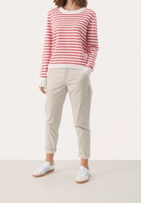 Rød og pinkstribet sweater med cremefarvede manchetter; beige chinos, opsmøgede ved kanten; hvide sneakers med lysebrune såler. Enkel, afslappet outfit.