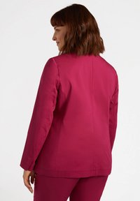 Giacca aderente in tessuto fucsia vivace. Presenta una texture liscia, maniche lunghe e un collo semplice. Schiena pulita con cuciture strutturate.