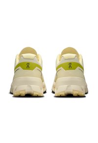 Beige és zöld sportcipők vastag talppal, sima textúrával, lekerekített formával és logóval a sarokrészen. A hátsó nézet a párnázottságot mutatja.