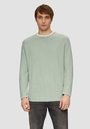 Lichtgroen overhemd met lange mouwen in een zachte textuur, met een ronde halslijn en contrasterende afwerking. Draagt het met donkergrijze jeans.