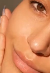 Nahaufnahme eines Gesichts mit Auge, Nase, Lippen und einer Hand, die sanft die Wange berührt.