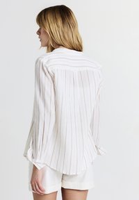 White and beige striped blouse with a relaxed fit, long sleeves, and a curved hem. Lightweight fabric with a textured finish.
