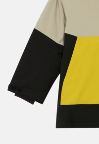 Krekla piedurkne un sānu ar krāsu blokiem, kas sastāv no bēšiem, melniem un dzelteniem paneļiem, melna regulējama rokas siksna un gludas auduma faktūra.