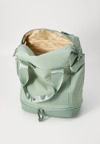 Mochila de color verde claro hecha de un tejido suave y texturizado. Cuenta con un cierre de cremallera, una gran apertura y un interior con un patrón beige. Incluye asas resistentes.